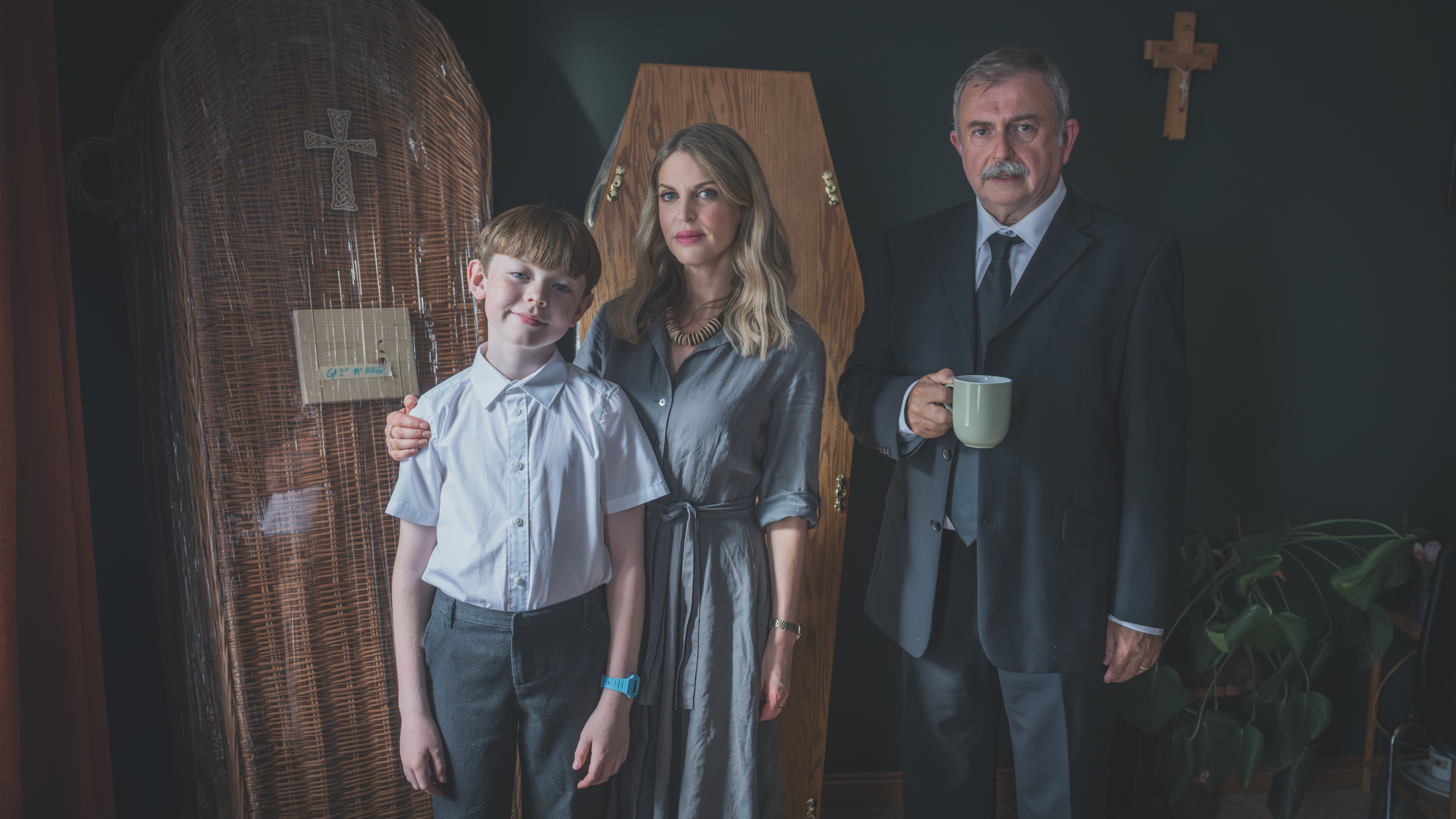 Main trio of cast standing against backdrop of Coffins